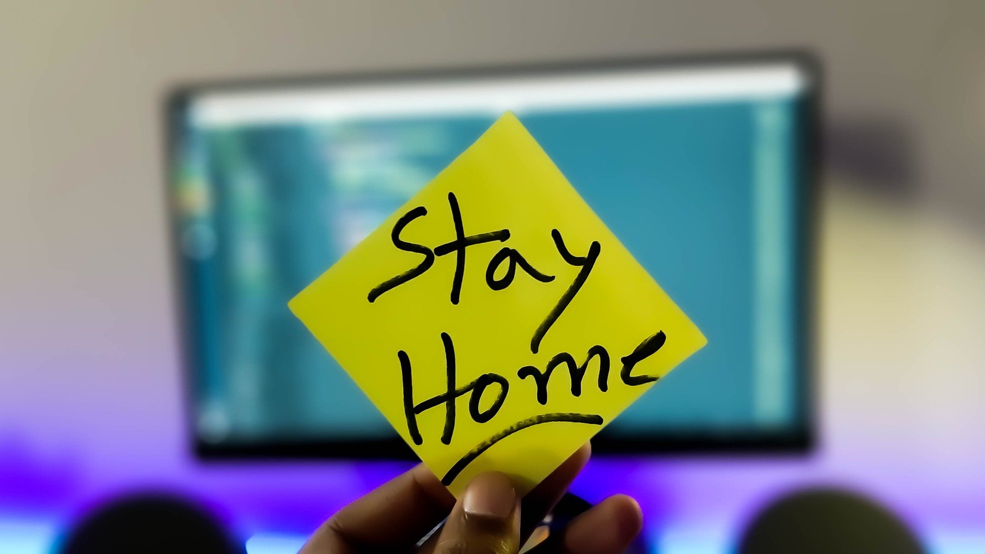 A hand holding a sticky note that says "Stay Home."