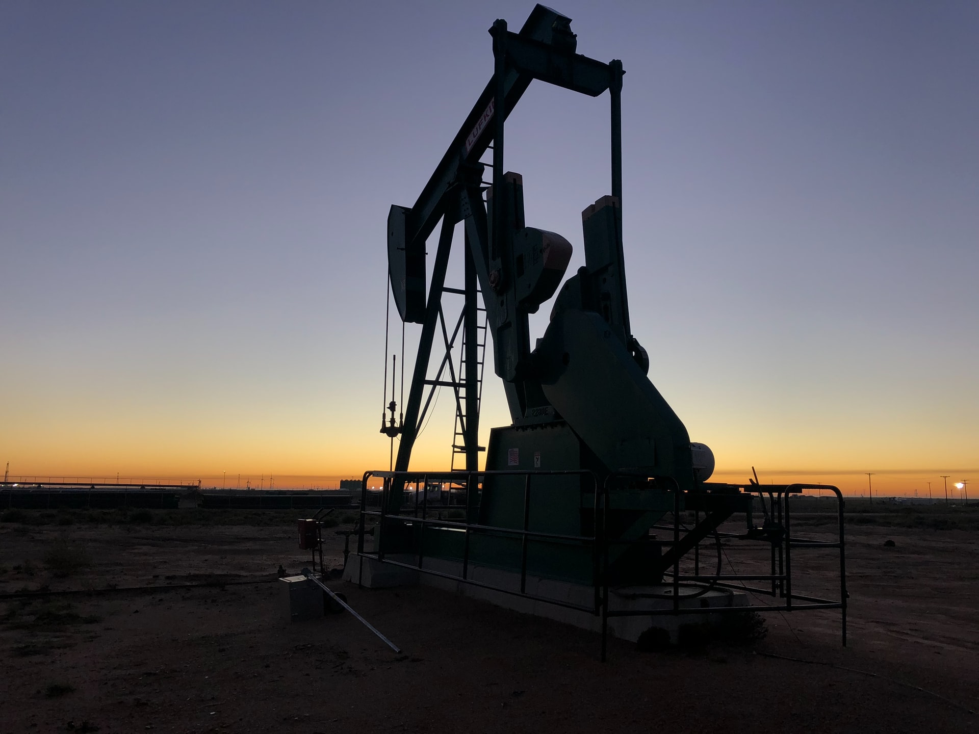 an oil derrick on a field at sunset