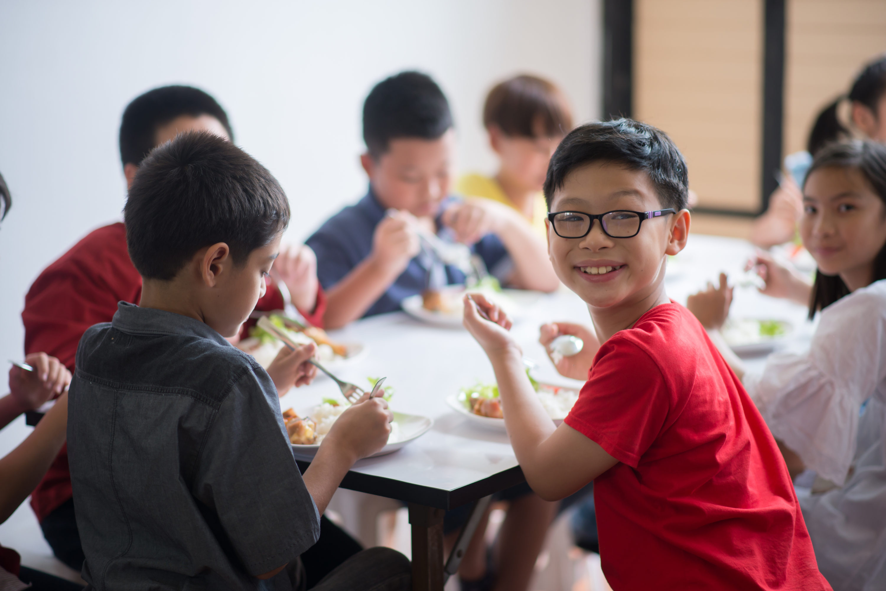 older elementary schoolchildren eating lunch, one is wearing glasses and smiling for the camera. Proposition FF